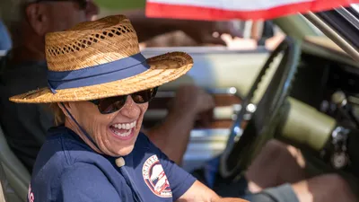 A woman in a straw hat laughs from behind the wheel of a classic car during the Fourth of July parade in Home, Washington.